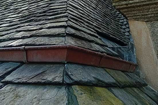 Photo d'un borde de toiture en ardoise avec une gouttière