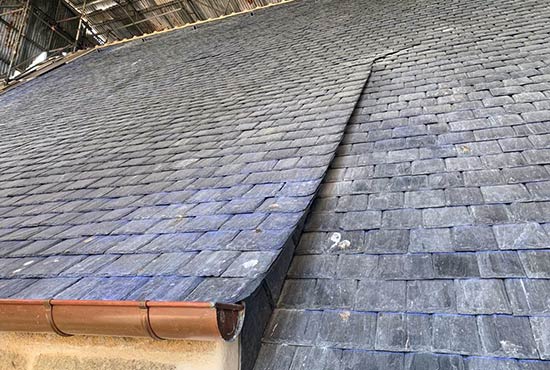 Photo d'un pan de toiture en ardoise avec gouttière en cuivre